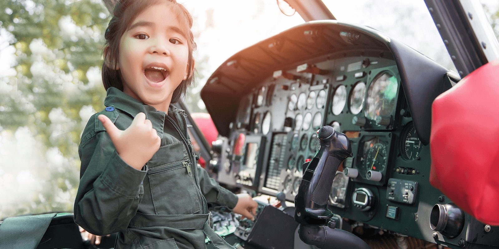 A young girl in a flight jumpsuit sitting at the controls of a military helicopter. 