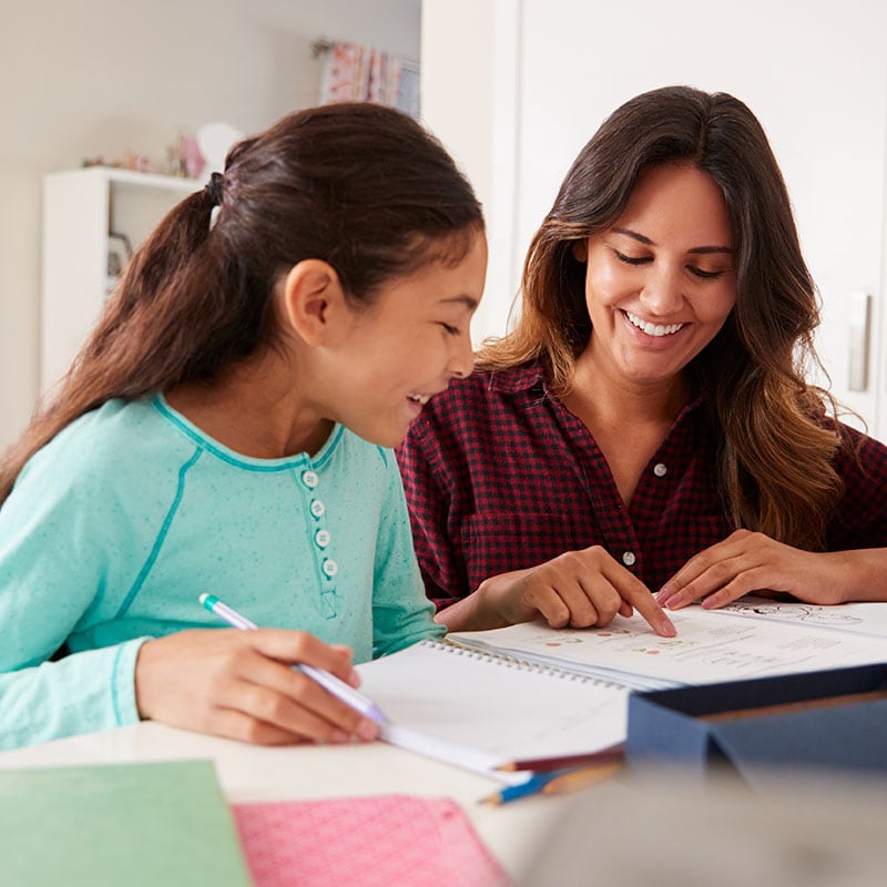 Mother helping her daughter with homework at the kitchen table. 