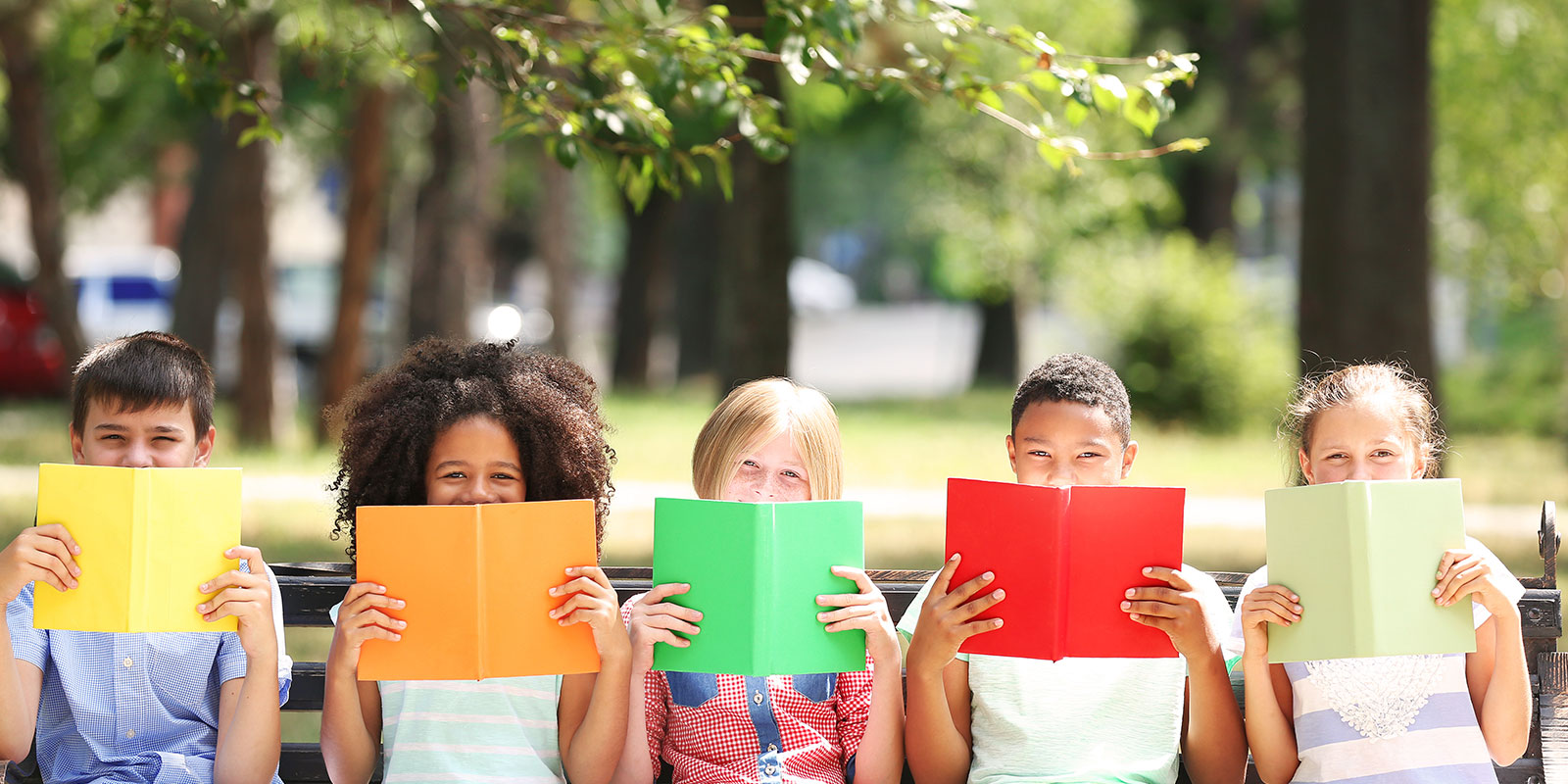 Young student sitting on a bench reading colorful books. 