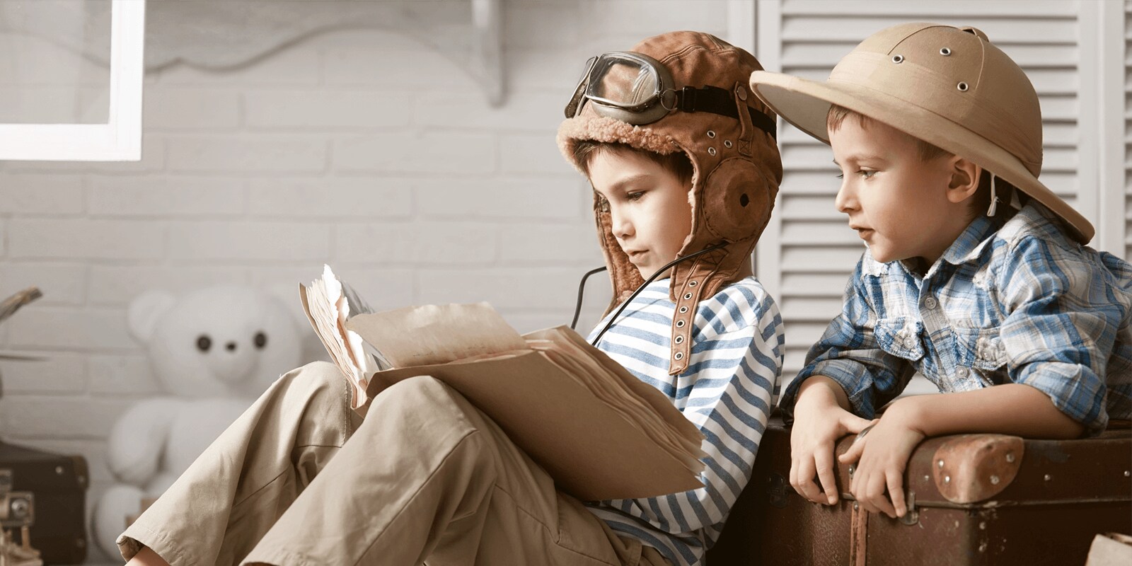 Two young boys sitting together. One wearting a flight helment and googles. 