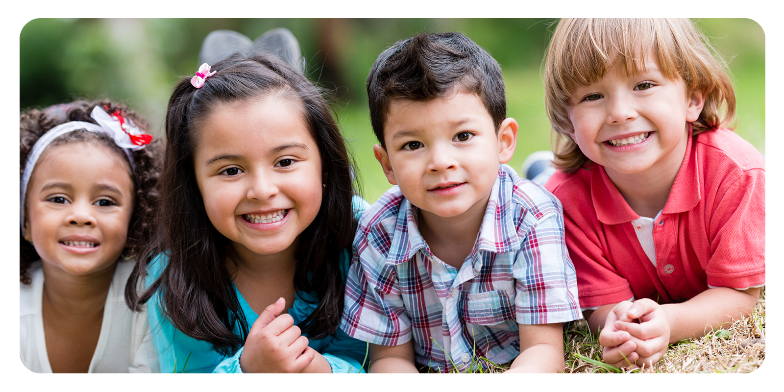 Four children sitting in the grass looking at the camera.