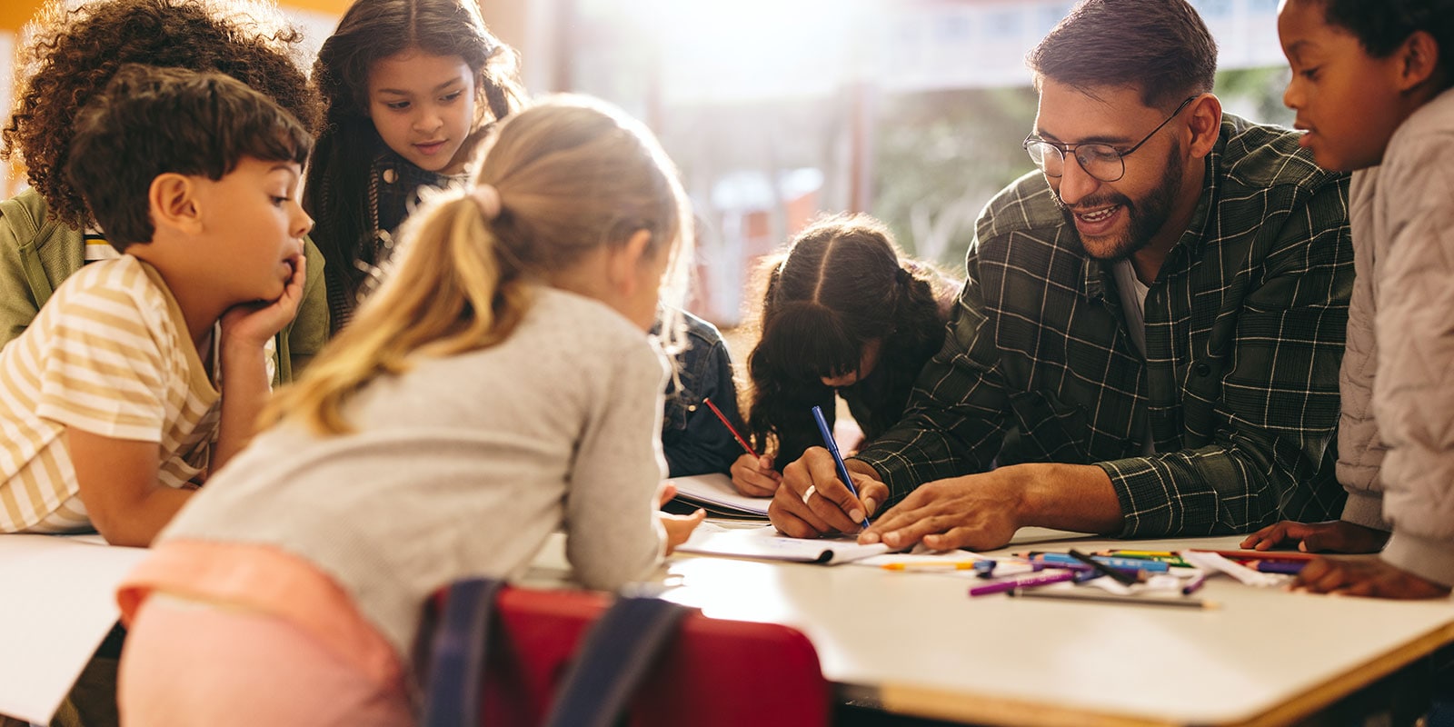 Male teacher with a group of young students at a table. 