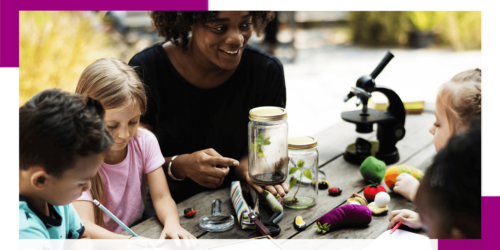 A teacher and four children engaged in a science activity at a wooden table outdoors.
