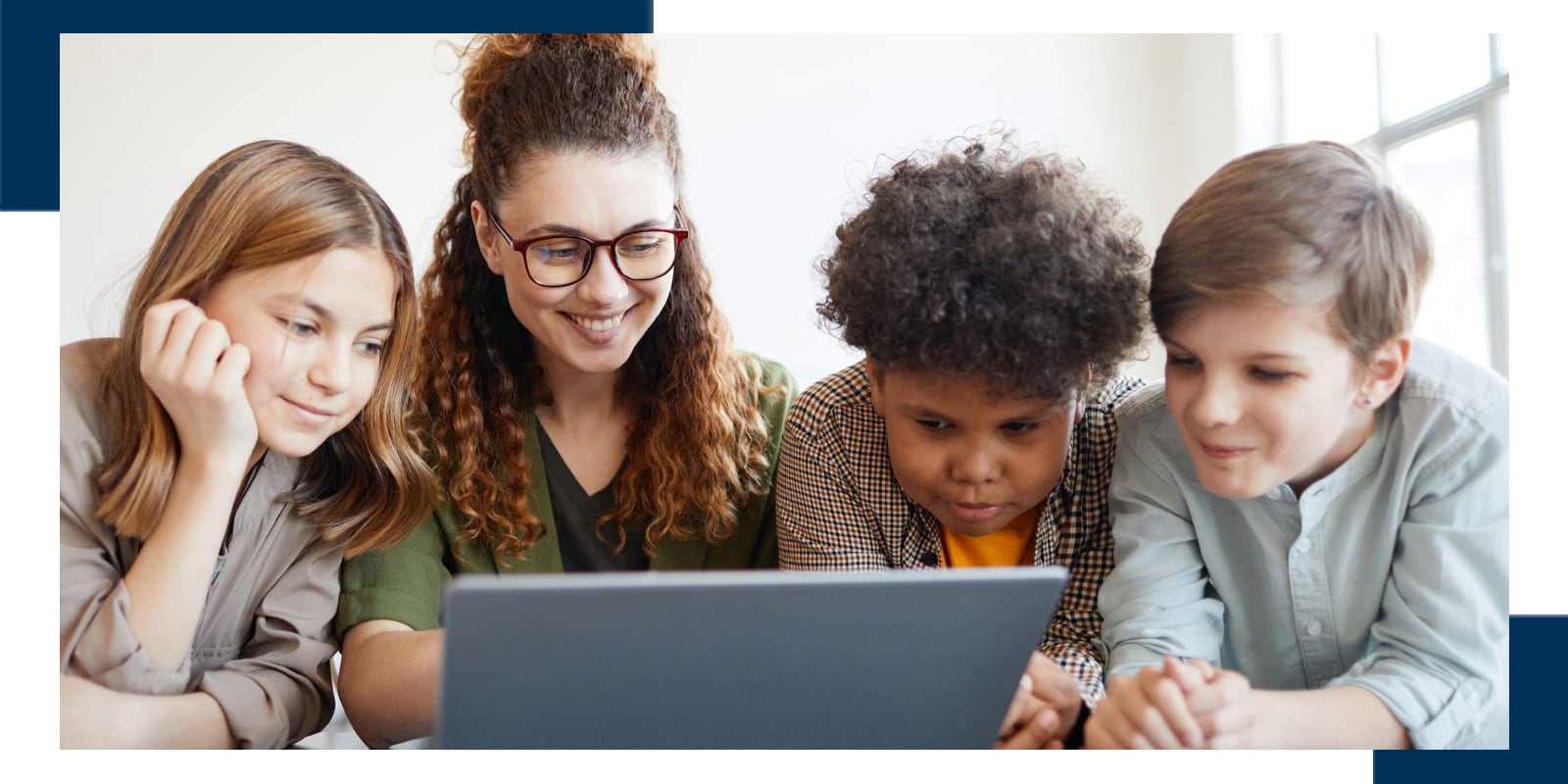 Smiling female teacher using computer with diverse group of children