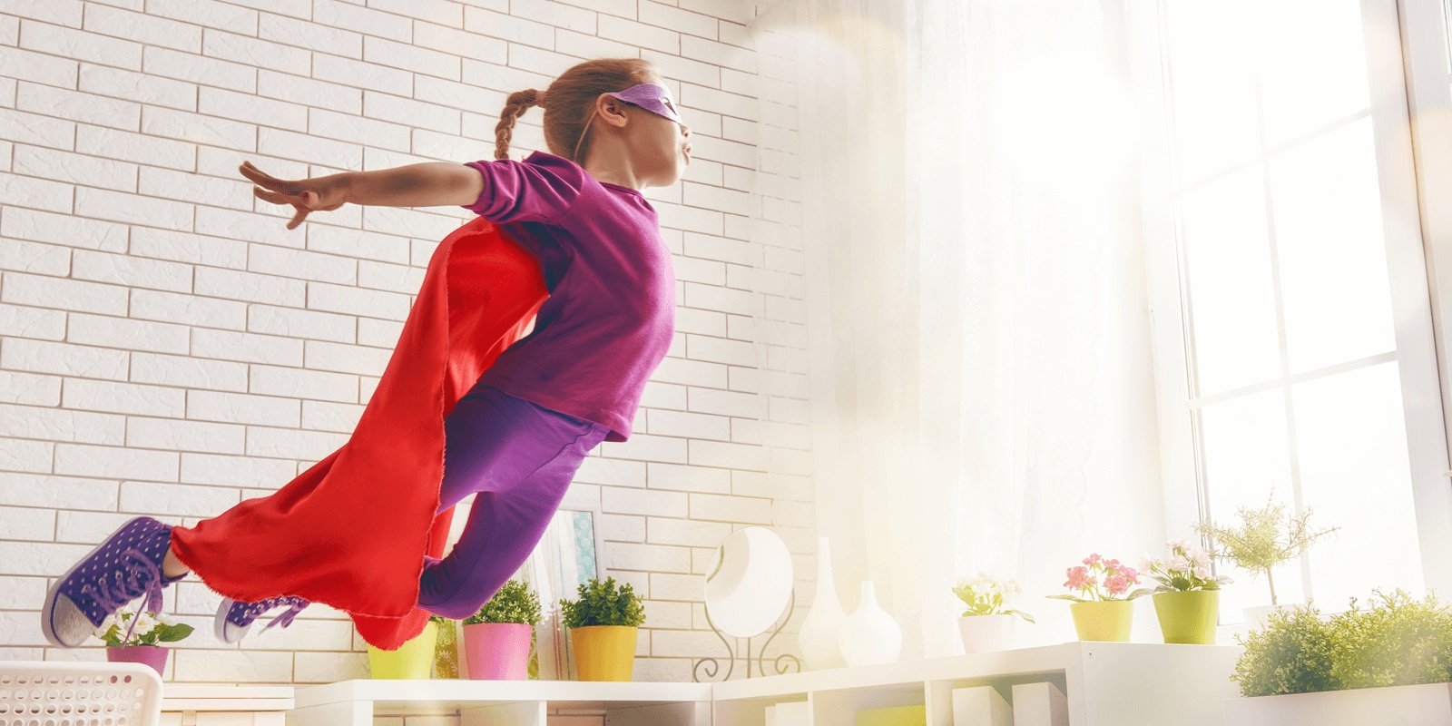 Child with super hero cape and mask over eyes jumping off furniture