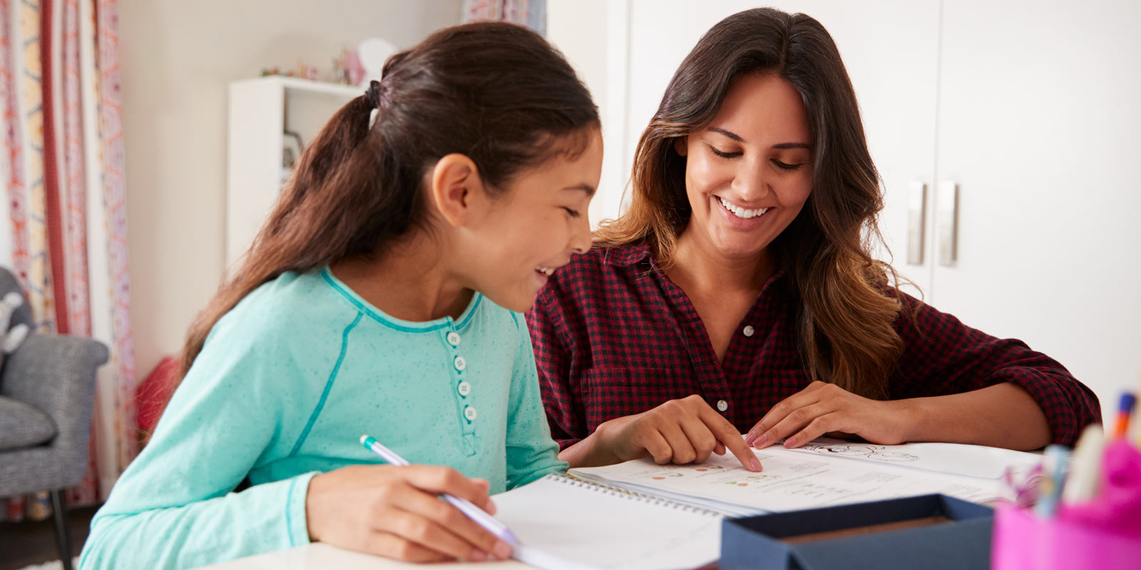 alt="A smiling adult assisting a smiling child with school work"
