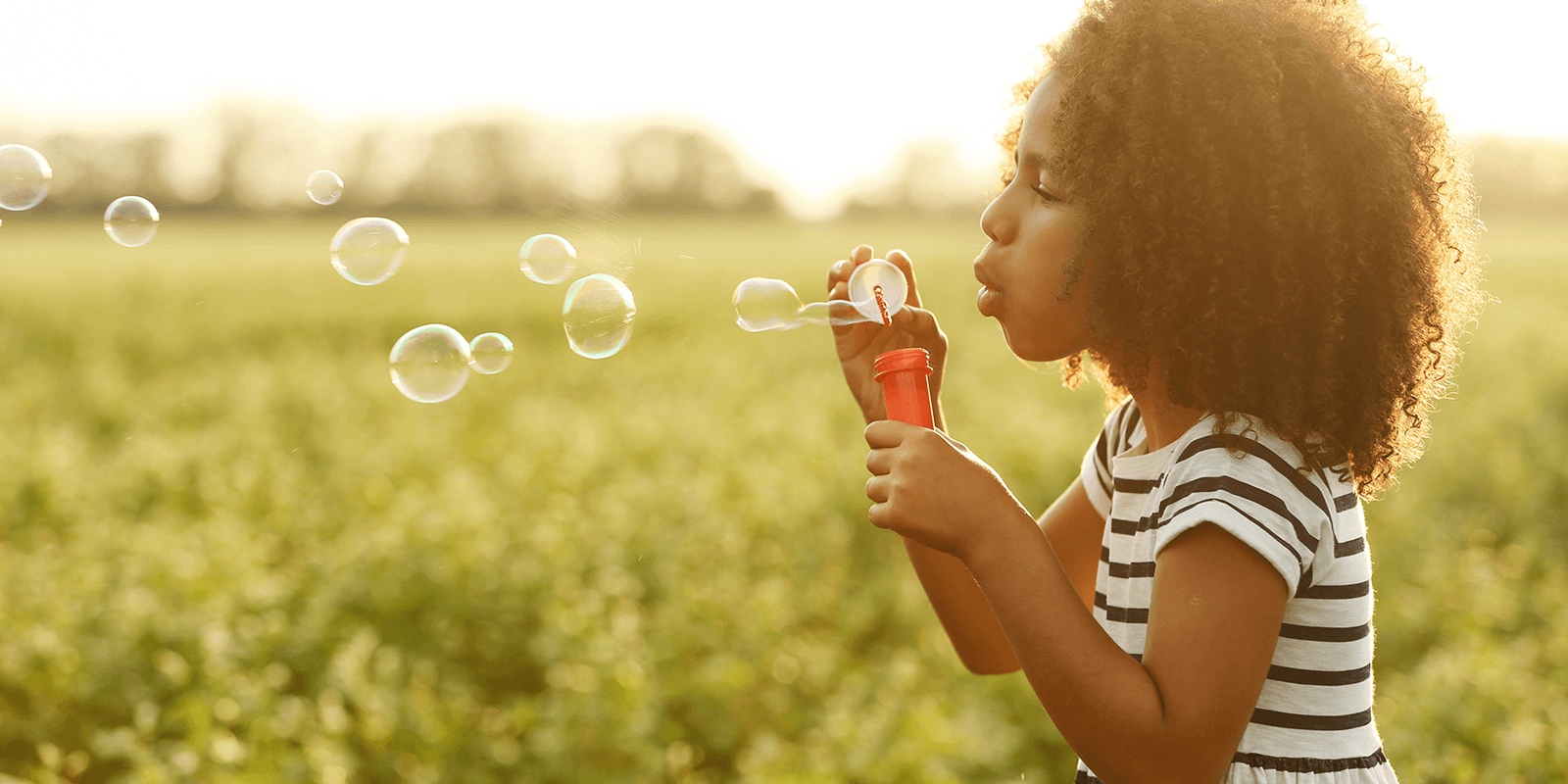 Young girls blowing bubbles in a grassy field at sunset.
