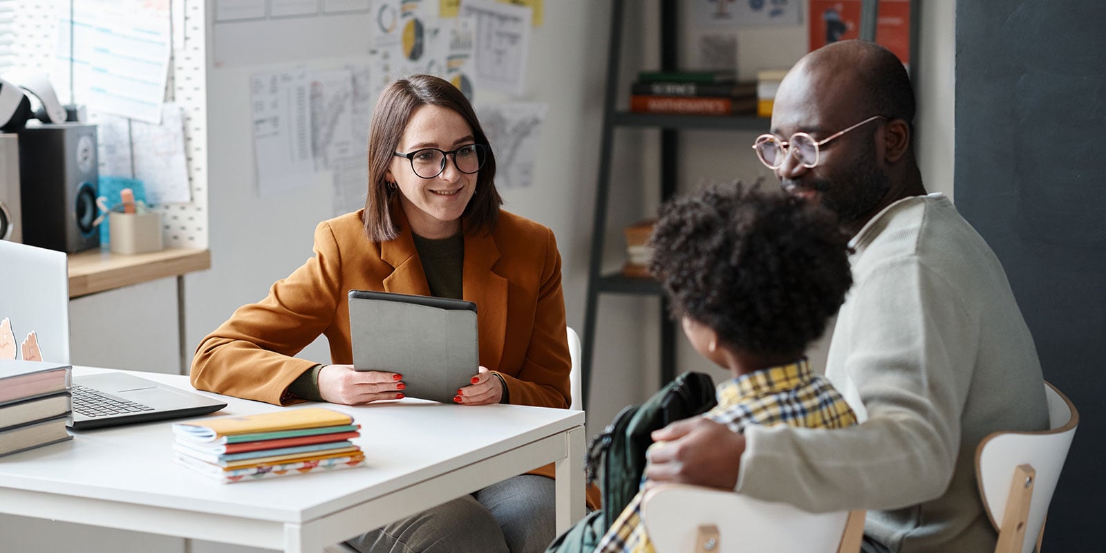 Teacher working with a young student in the classroom while the father is present. 