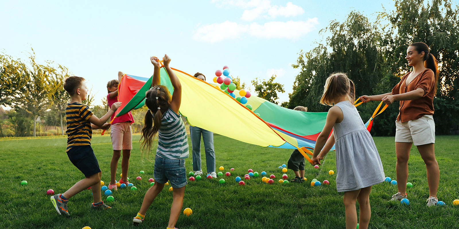 Female teacher working with young children outside playing ball.