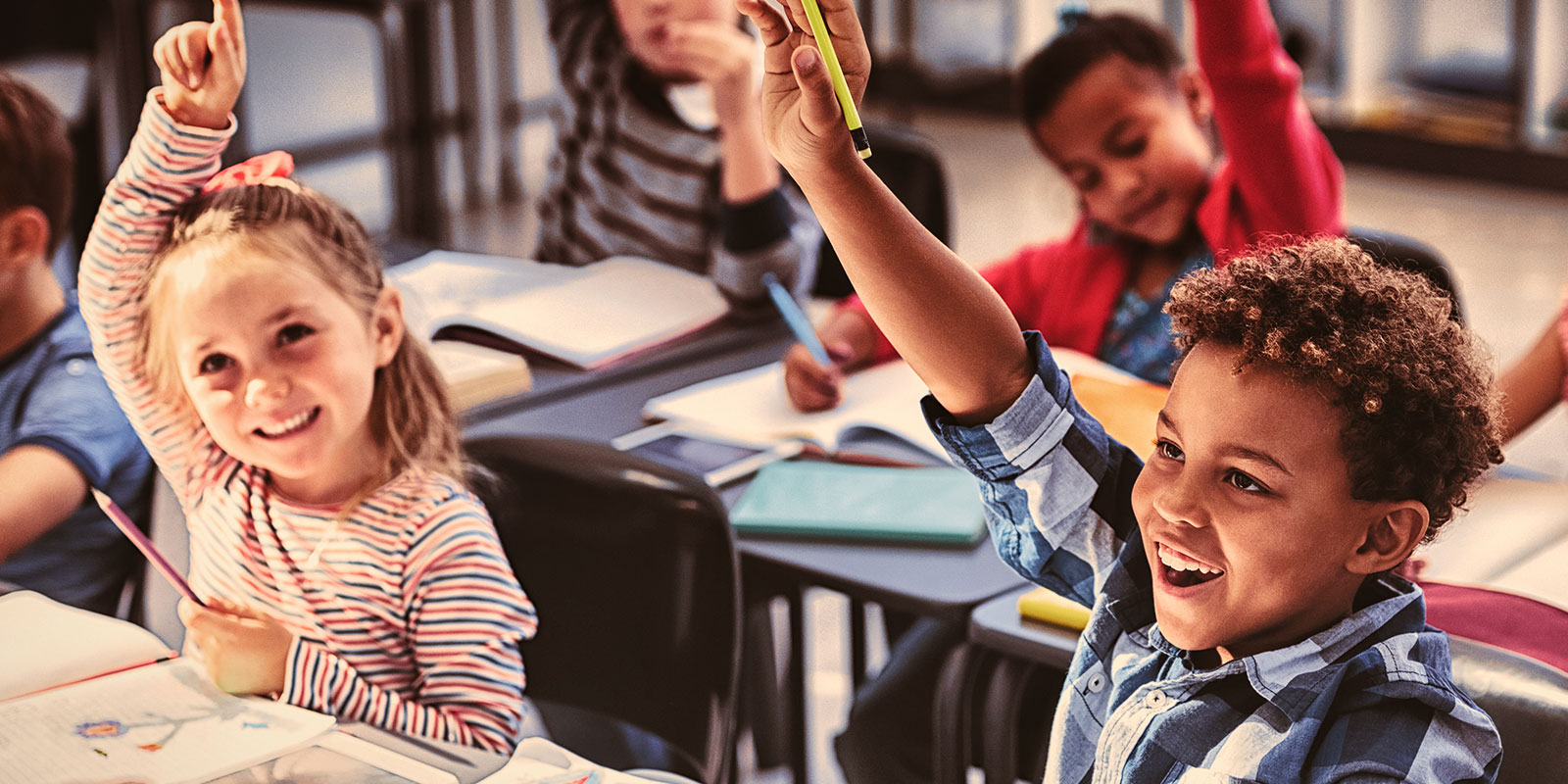 Two young students raising their hand in class. 
