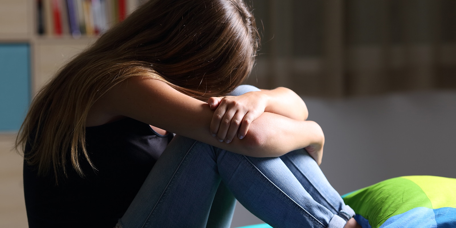 Teen aged girl sitting alone with her head in her lap. 